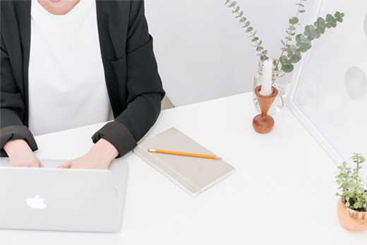 Person typing on laptop with notepad beside them